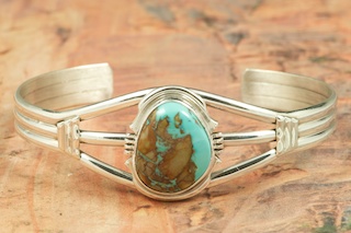 Genuine Boulder Turquoise set in Sterling Silver Bracelet. The cabochon is Boulder Turquoise, you can see the veins of Turquoise running through the host rock. The Boulder Turquoise Mine is located in northeast Nevada. It was discovered in 1970 by a Shoshone sheep herder. Production is small due to the remote location and winter weather. Boulder Turquoise is valued for both it's beauty and rarity. Every stone is unique. Created by Navajo Artist Arkie Nelson. Signed by the artist. 
